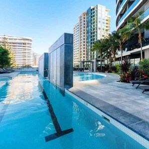 Ein Swimmingpool mit einer Tiefenmarkierung von 12 Metern, umgeben von modernen Gebäuden und Palmen.
