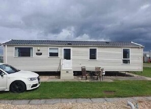 Ein Bungalow mit Eingangstür, zwei Fenstern und einer kleinen Terrasse mit Tisch und Stühlen.