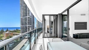 A balcony with a glass railing, a dining table, and a view of the ocean and buildings. - Beach Fun at Oracle Level 10 (Gold Coast)