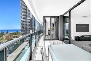 Ein Balkon mit Glasgeländer, einem Esstisch und Blick auf das Meer und Gebäude.