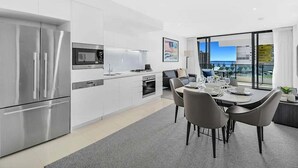 A modern kitchen with stainless steel appliances, a dining area with a table and chairs, and a view of the city through large windows. - Beach Fun at Oracle Level 10 (Gold Coast)