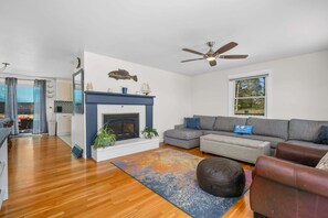 Ein Wohnzimmer mit Kamin, Deckenventilator, grauem Sofa und Holzboden.
