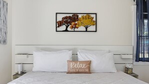 A bed with white bedding, a pillow with 'Relax You're on beach time' text, and a wall art of autumn trees. - Peaceful Stay with Town Cove Access (Eastham)