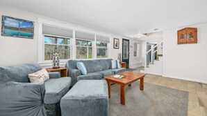 A living room with a sectional sofa, a wooden coffee table, and a large window with a view of trees. - Peaceful Stay with Town Cove Access (Eastham)