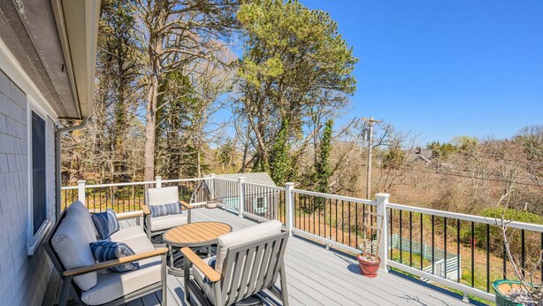 A deck with outdoor furniture, a railing, and a view of trees and a house. - Peaceful Stay with Town Cove Access (Eastham)