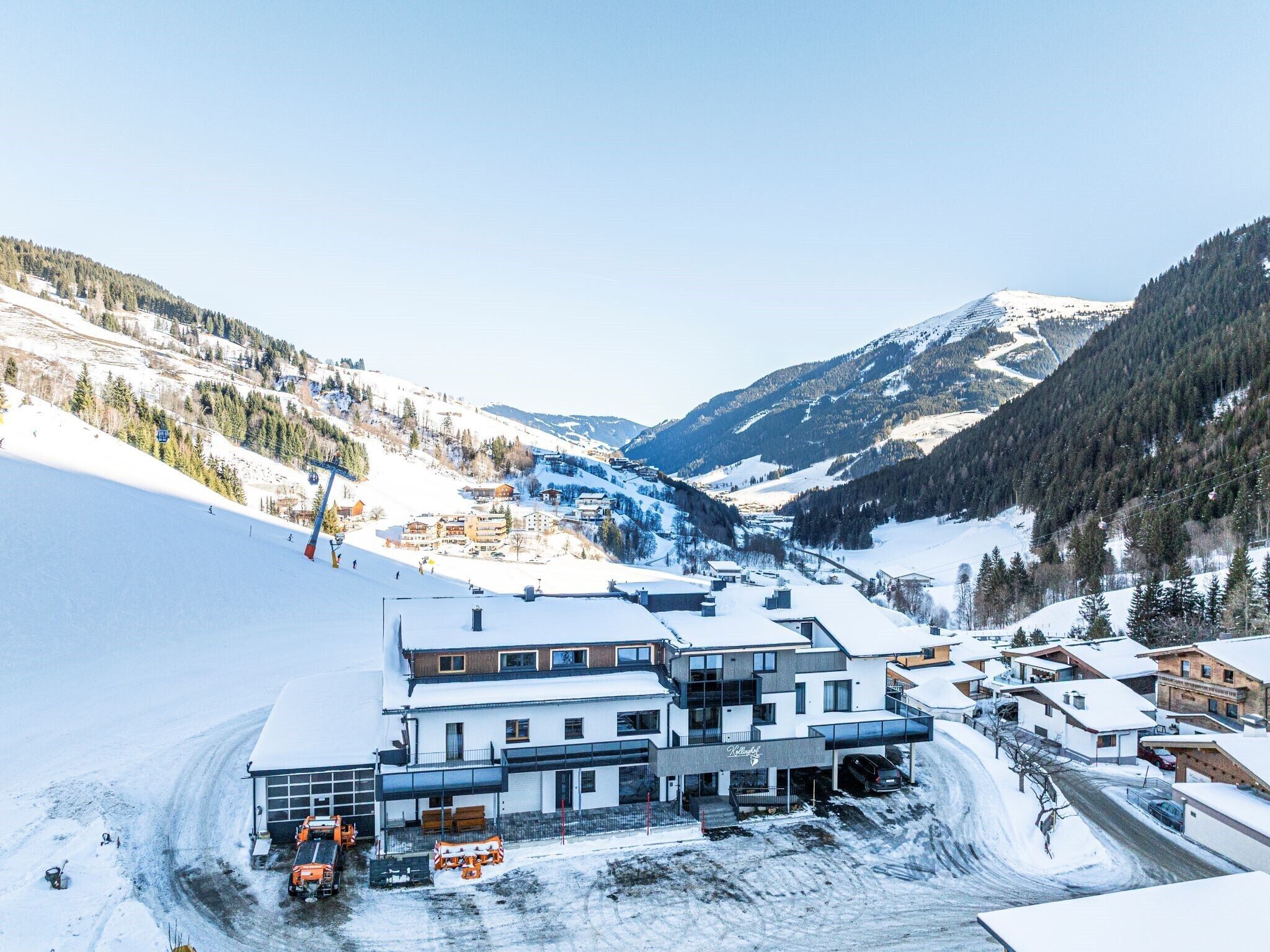 Un hotel moderno con una seggiovia sullo sfondo, circondato da montagne innevate.