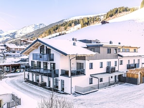 Ein modernes, zweistöckiges Gebäude mit großen Fenstern, einem Balkon und einer verschneiten Landschaft.