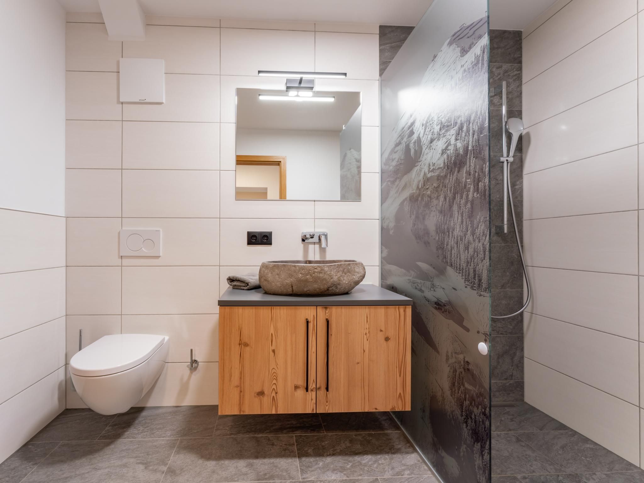 Un baño moderno con tocador de madera, lavabo redondo, inodoro y zona de ducha.