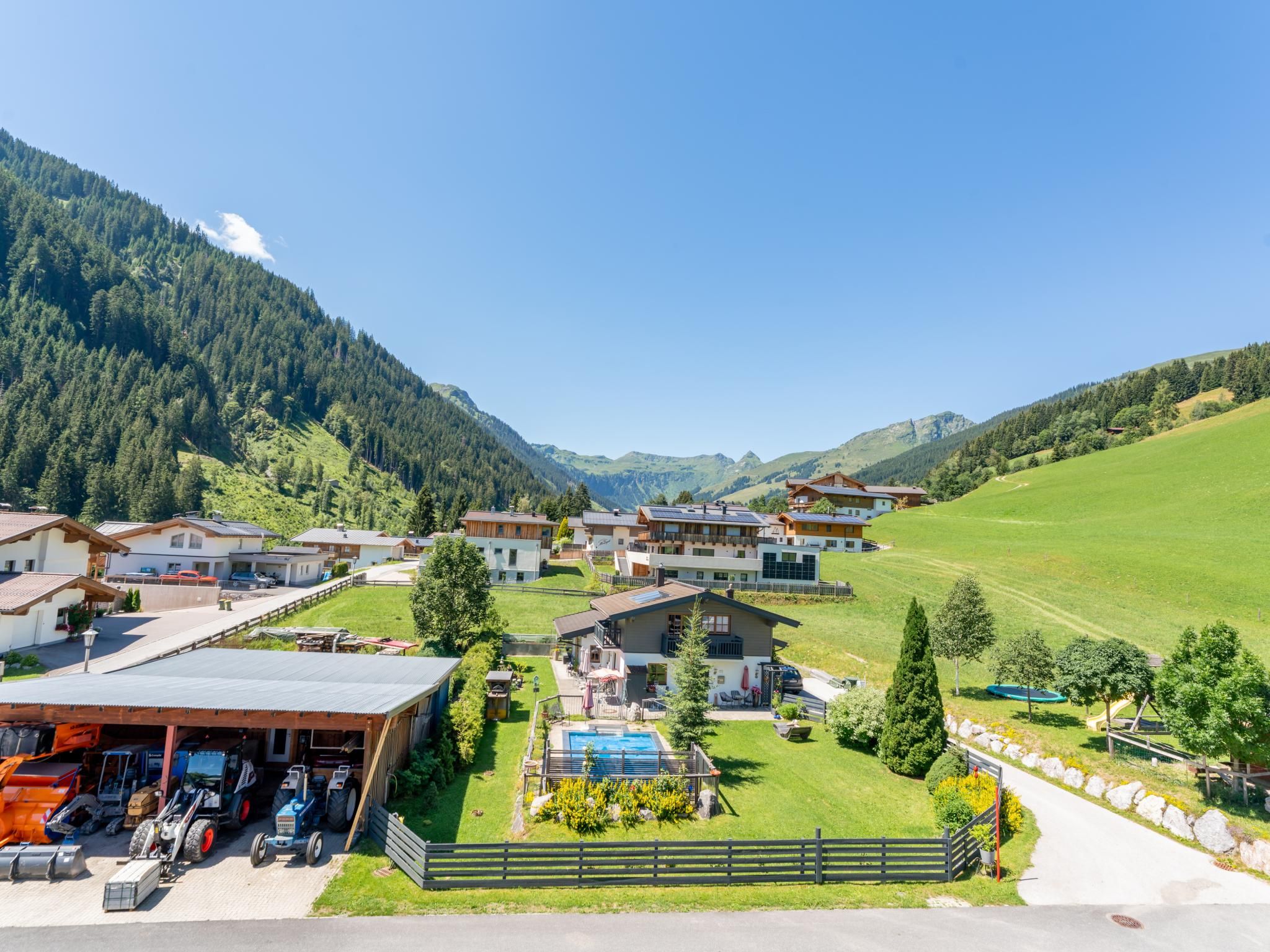 A mountain village with houses, a swimming pool, and a tractor.