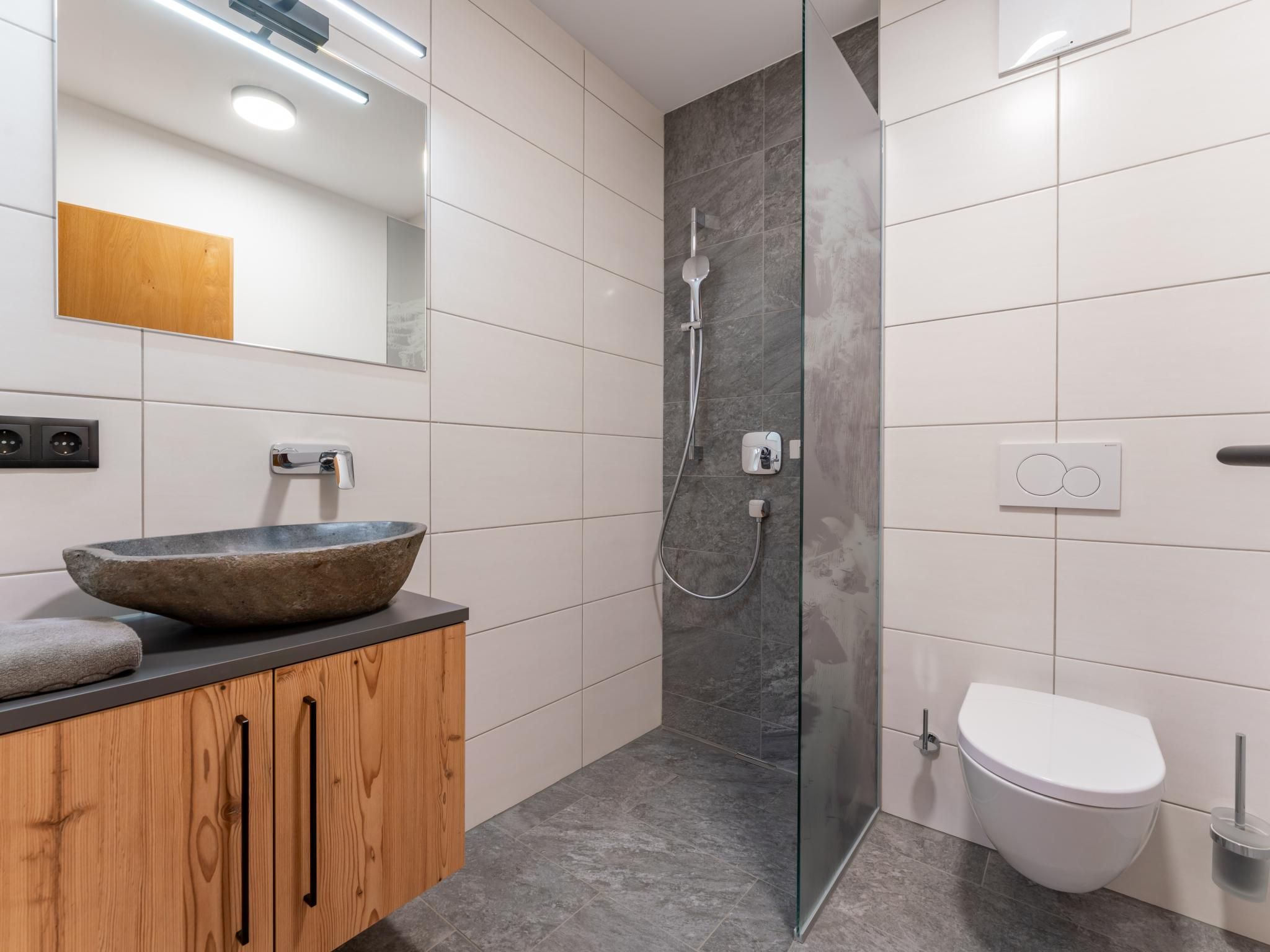 Un baño moderno con un lavabo de piedra, un mueble de madera, cabina de ducha con mampara de vidrio y un inodoro.