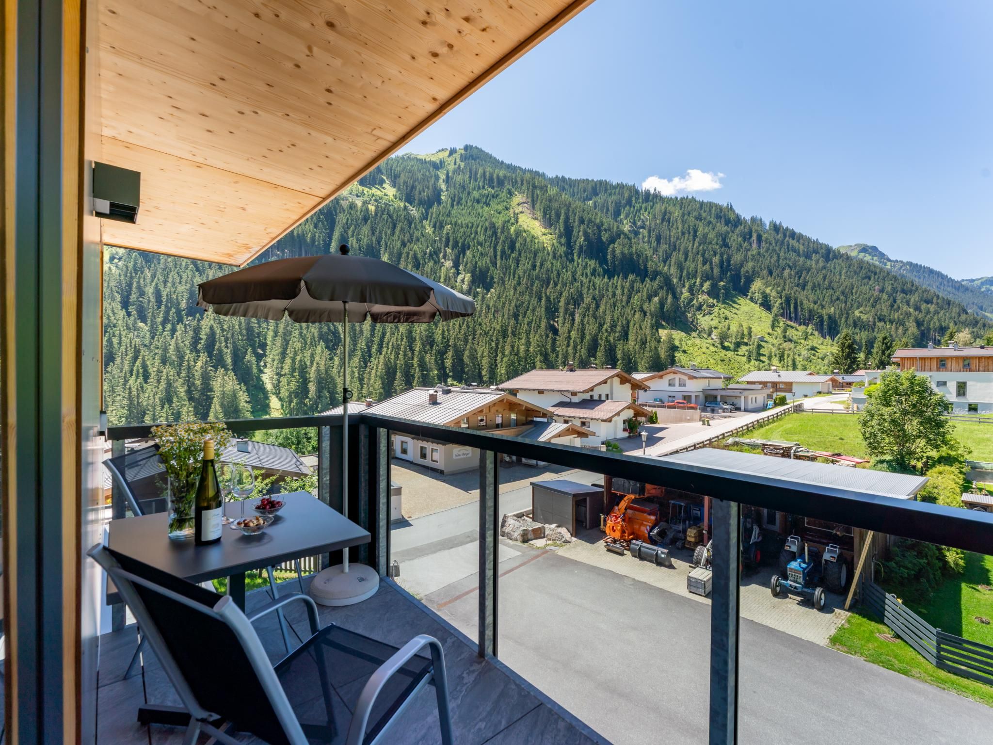 Un balcon avec une table, des chaises et un parasol, donnant sur un paysage montagneux parsemé de bâtiments.