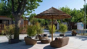 An outdoor seating area with wicker furniture and a thatched umbrella. - Holiday apartment with wooden veranda (Viserba di Rimini)