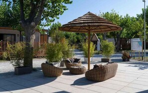 An outdoor seating area with wicker furniture and a thatched umbrella. - Holiday apartment with wooden veranda (Viserba di Rimini)