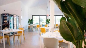 A spacious indoor area with tables and chairs, large windows, and potted plants. - Holiday apartment with wooden veranda (Viserba di Rimini)