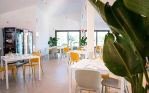A spacious indoor area with tables and chairs, large windows, and potted plants. - Holiday apartment with wooden veranda (Viserba di Rimini)