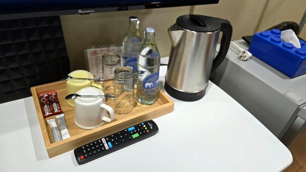 A kitchen counter with a coffee maker, bottles, glasses, a remote control, and a tray with snacks.