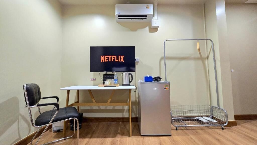 A room with a desk, chair, TV, refrigerator, and a metal cart.