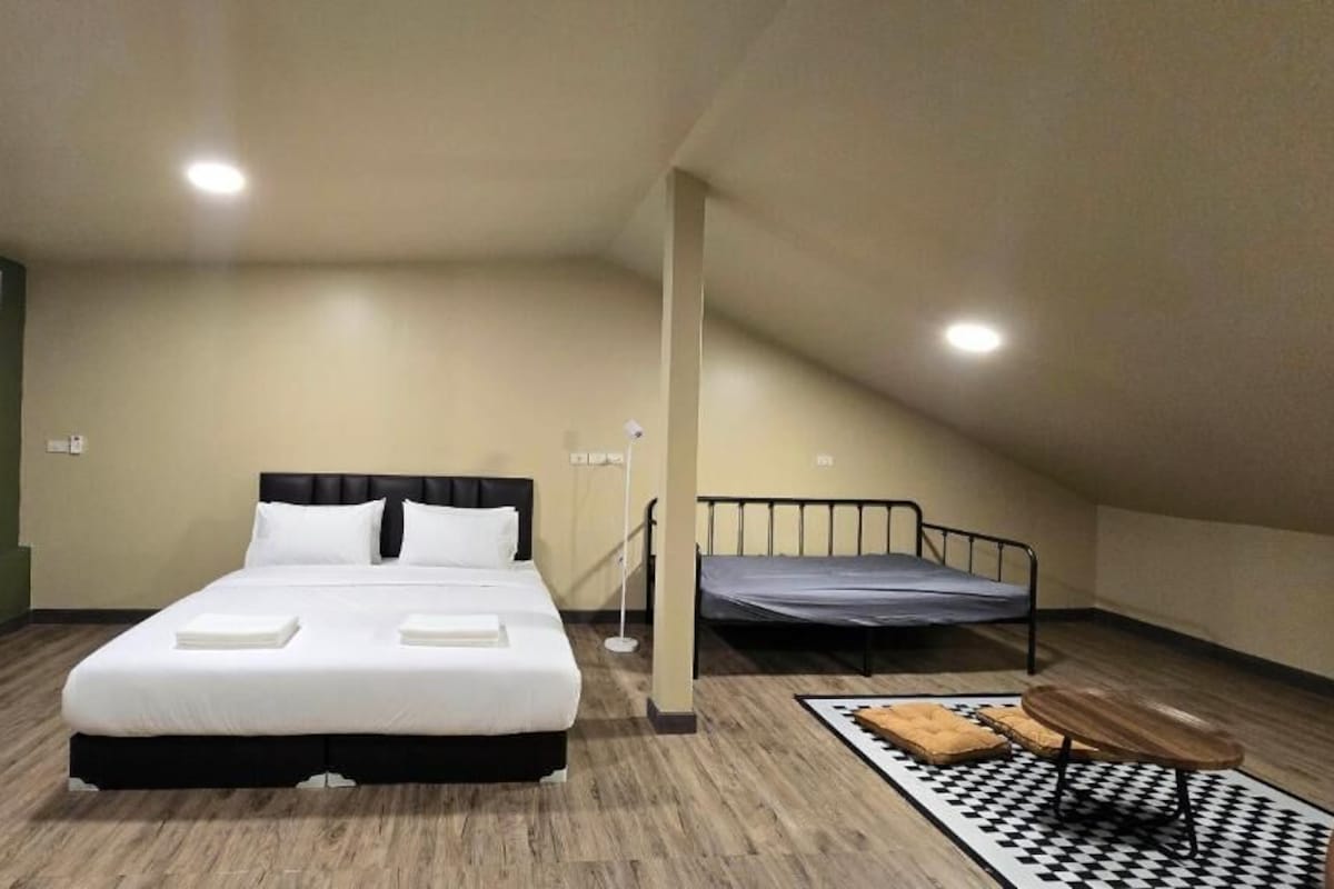 A single bed with a black frame, a small table, and a chair in a room with wooden flooring and a sloped ceiling.
