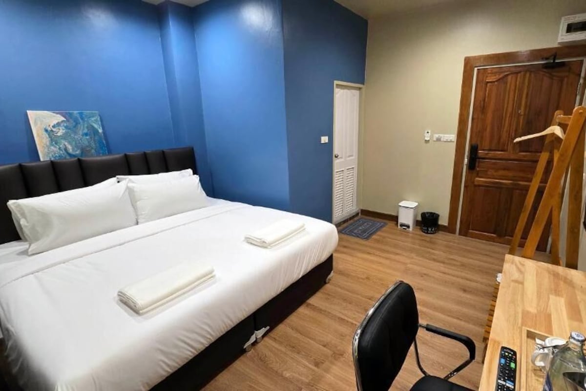A hotel room with a bed, a desk with a computer, a TV, and a door.