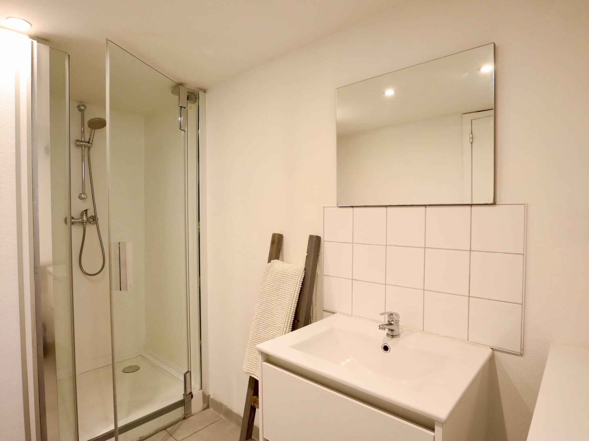 A bathroom with a glass shower enclosure, a white sink with a mirror above it, and a tiled wall.