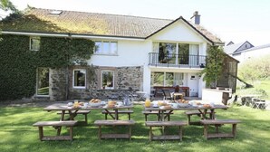 A two-story house with a stone facade, a balcony, and a patio area with picnic tables set up for outdoor dining. - Large cottage near the Fagnes and Francorchamps. (Francorchamps)