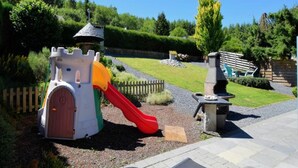 Une aire de jeux avec une structure en forme de château, un toboggan et un espace barbecue.