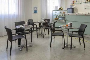 Ein Essbereich mit runden Tischen und Stühlen, einem Kühlschrank und einer Vitrine mit Lebensmitteln.