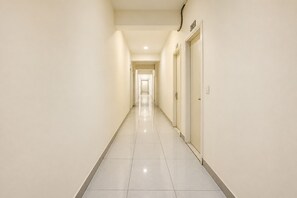 A long, narrow hotel corridor with doors on one side and a tiled floor. - Aerohub Suites: Himalayan Foothills Escape Cozy 1BHK in Zirakpur, NearChandigarh (Zirakpur)
