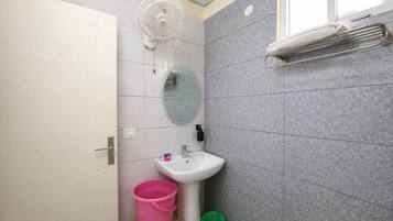Ein Badezimmer mit einem weißen Waschbecken, einem runden Spiegel, einem weißen Ventilator, einem Handtuchhalter und einem Fenster.