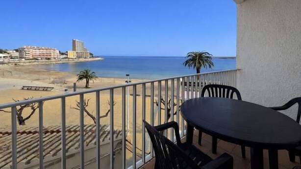 Ein Balkon mit Blick auf den Strand, einem Tisch, Stühlen und einem Geländer.