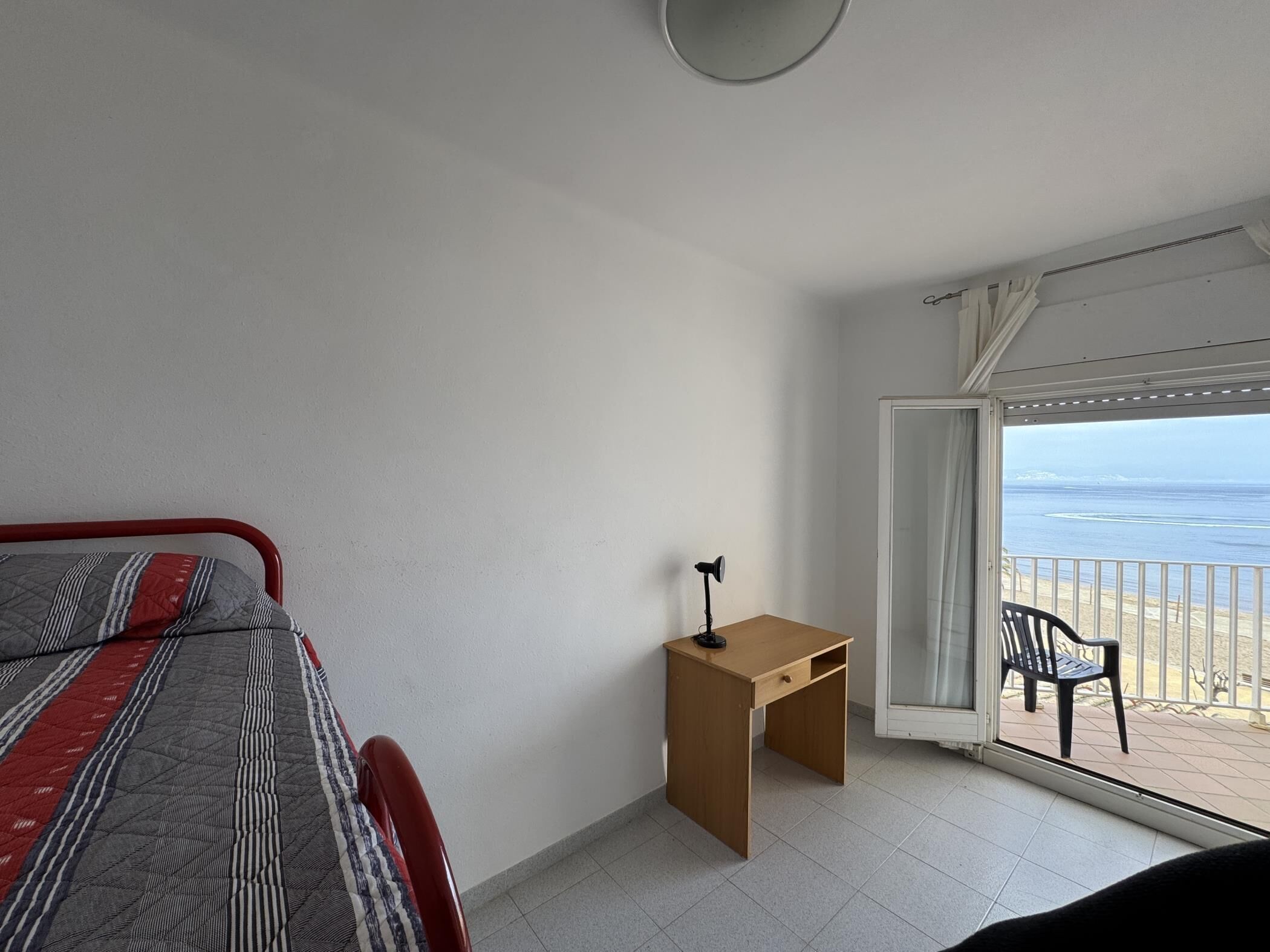 Un dormitorio con cama, escritorio y balcón con vista al mar.