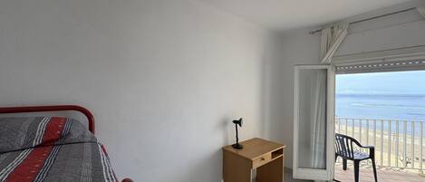 Un dormitorio con cama, escritorio y balcón con vista al mar.