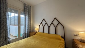 Ein Schlafzimmer mit Bett, Nachttisch, Lampe und einem Fenster mit Vorhängen.