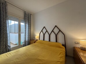 A bedroom with a bed, a nightstand, a lamp, and a window with curtains. - Second-floor apartment with privileged sea views (l'Escala)