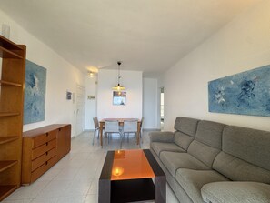 Un salon comprenant un canapé, une table basse, une table à manger avec des chaises, un meuble en bois et deux tableaux abstraits accrochés aux murs.