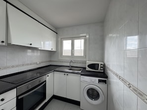 Une cuisine compacte équipée d’un lave-linge, d’un four à micro-ondes et d’un évier.