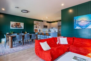 Ein modernes Wohnzimmer mit einem roten Sofa, einem Essbereich und einer Küche im Hintergrund.