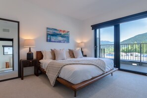 Ein Schlafzimmer mit einem großen Bett, zwei Nachttischen, einem Gemälde und einem Balkon mit Blick.