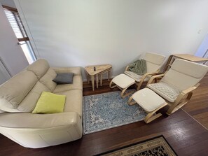 A living room with a beige sofa, two wooden chairs, a small wooden table, and a blue patterned rug.