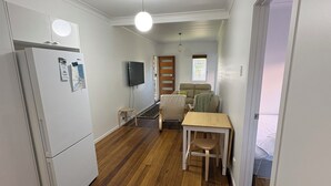 Et kompakt køkken med et køleskab, et spisebord med stole, en sofa og et fjernsyn.