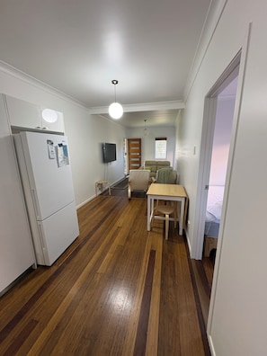 A compact kitchen with a refrigerator, a dining table with chairs, a sofa, and a television.
