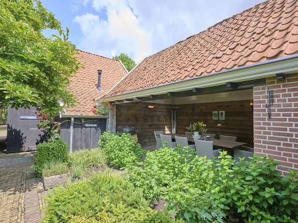 A covered patio with outdoor seating, a brick wall, and a garden area with various plants.
