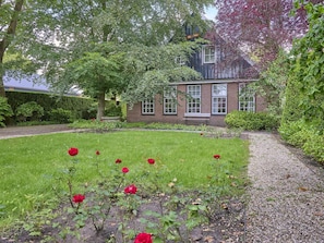 A garden with a lawn and red roses, a brick building with windows, and a hedge.