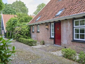 A brick house with a red door, a small garden, and a cobblestone path.