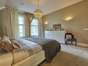 A bedroom with a bed, a dresser, a chair, a hanging light fixture, and a painting on the wall.