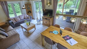 A cozy living room with a sofa, coffee table, TV, and dining area with chairs and a table. - Home in a private park with a spacious garden (Epe)