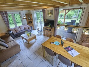 A cozy living room with a sofa, coffee table, TV, and dining area with chairs and a table. - Home in a private park with a spacious garden (Epe)