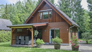 A wooden house with a covered porch, a garage, and a garden with potted plants. - Home in a private park with a spacious garden (Epe)
