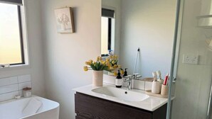 A modern bathroom with a bathtub, a sink, a mirror, and a shower. - Bedroom (Jack's Point)