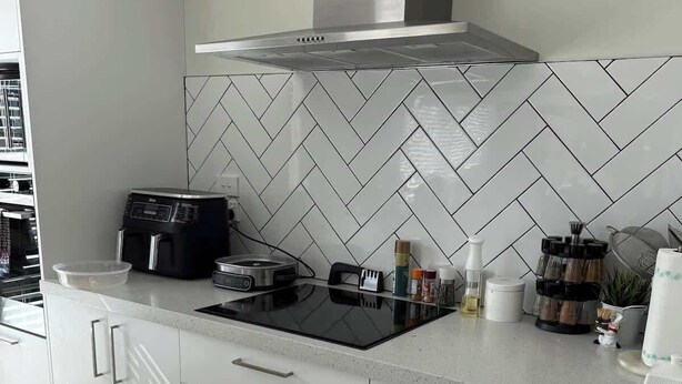 A modern kitchen with a herringbone tile backsplash, a built-in oven, and a stainless steel range hood. - Bedroom (Jack's Point)